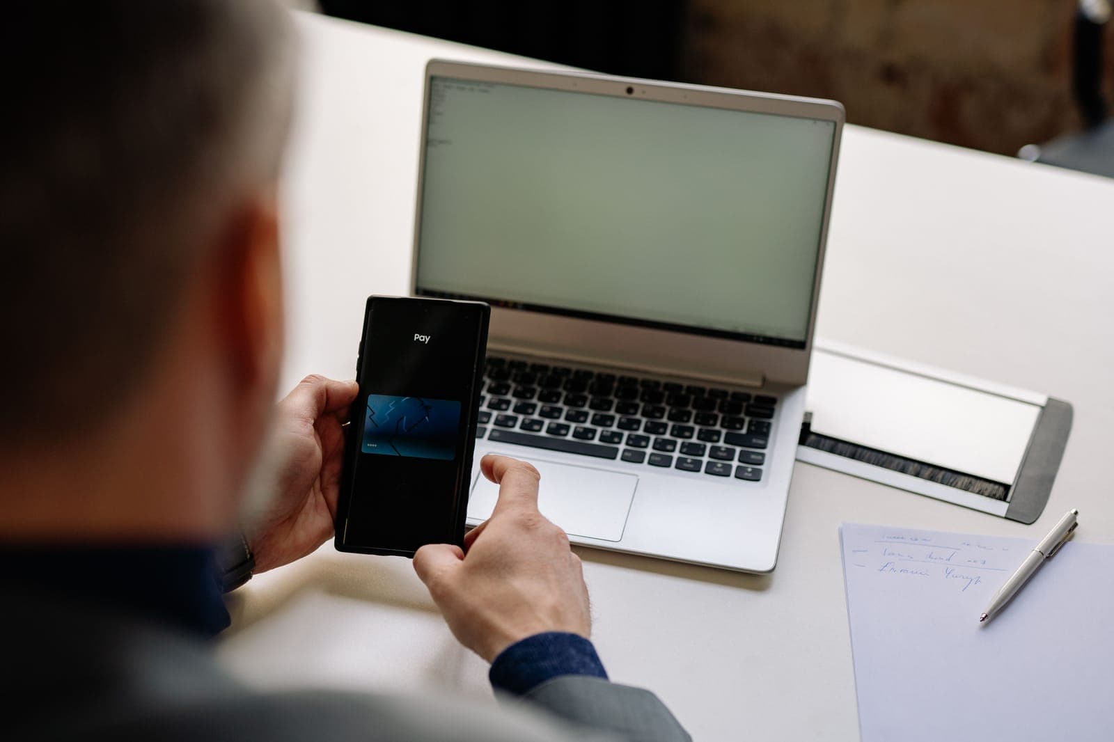Mann bezahlt am Schreibtisch per Smartphone