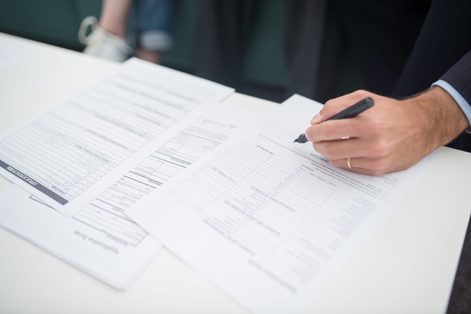 Hand unterschreibt Vertragsunterlagen auf einem Tisch
